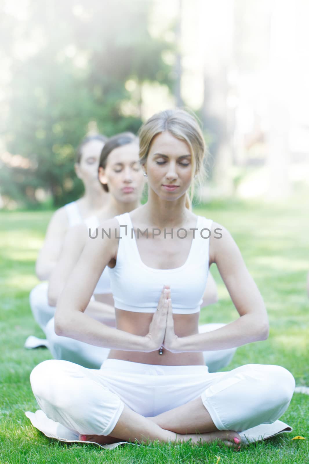 Women in white sportswear sitting in lotus position during group yoga training at park