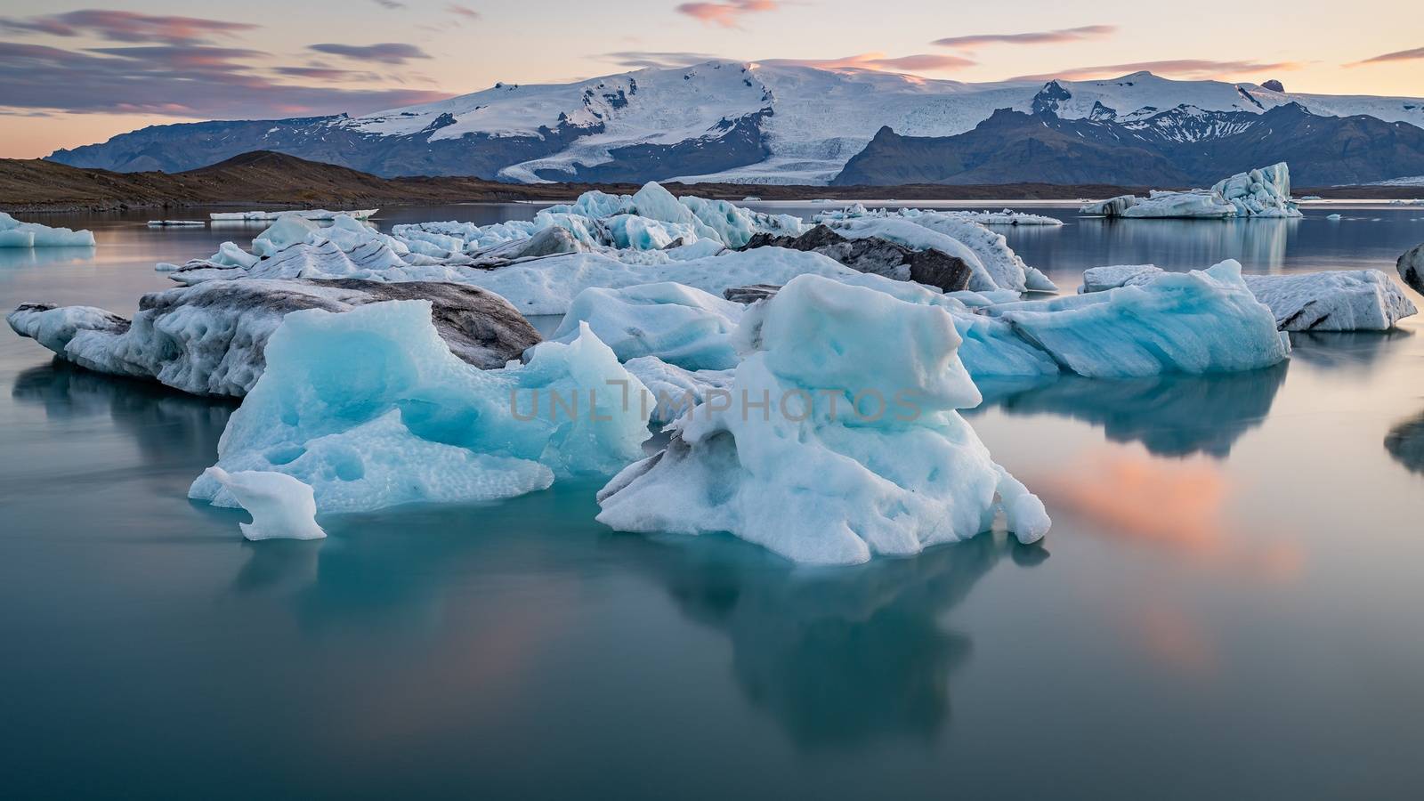 Little red sailboat cruising among floating icebergs in Disko Bay glacier during midnight sun season of polar summer. Ilulissat, Greenland. by bhavik_jagani