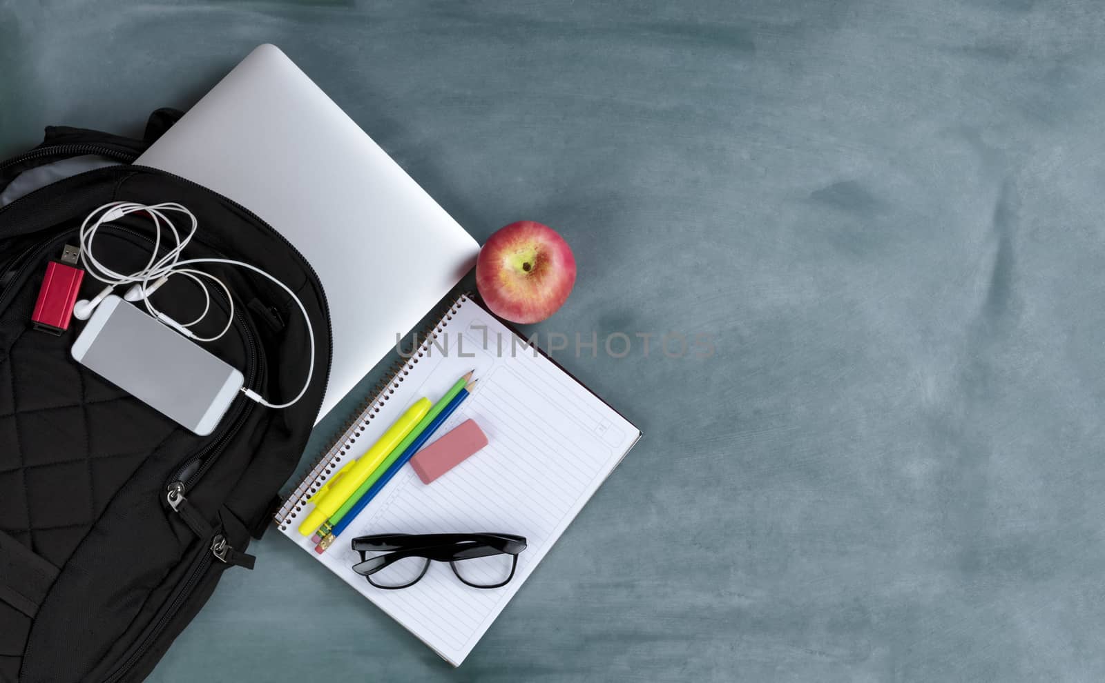 Back to school concept with basic modern technology and traditional educational objects on erased green chalkboard background