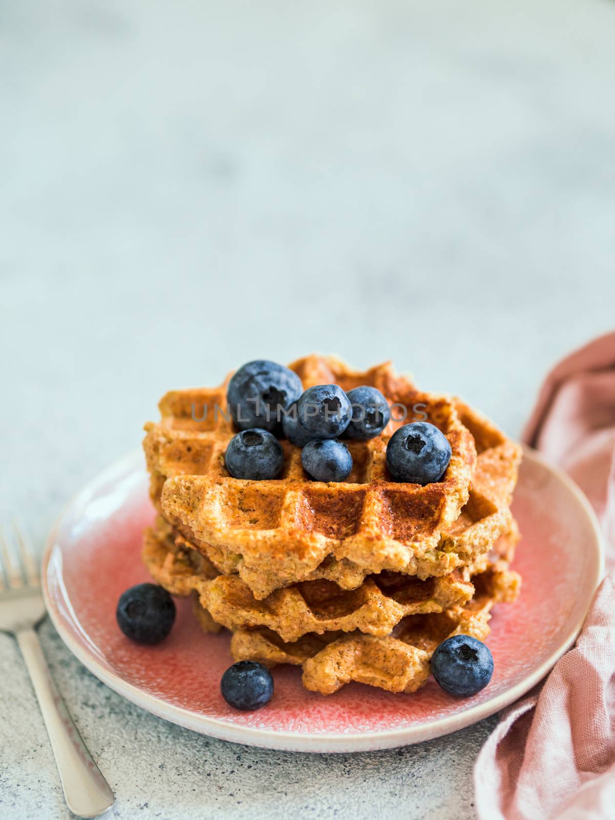 Easy healthy gluten free oat waffles with copy space. Stack of appetizing homemade waffles with oat flour decorated blueberries, on plate over light gray cement background. Vertical