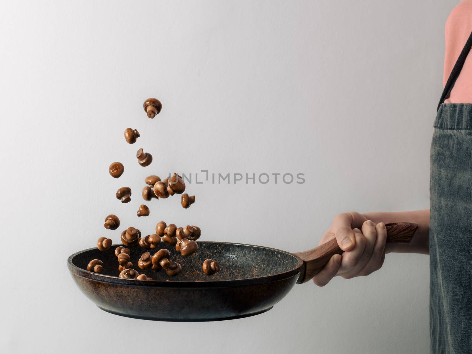 Chef woman preparing mini champignons in skillet frying them. Flying ingredients over pan with copy space. Hotel and caternig business, menu in restaurants, book of recipes concept. White background