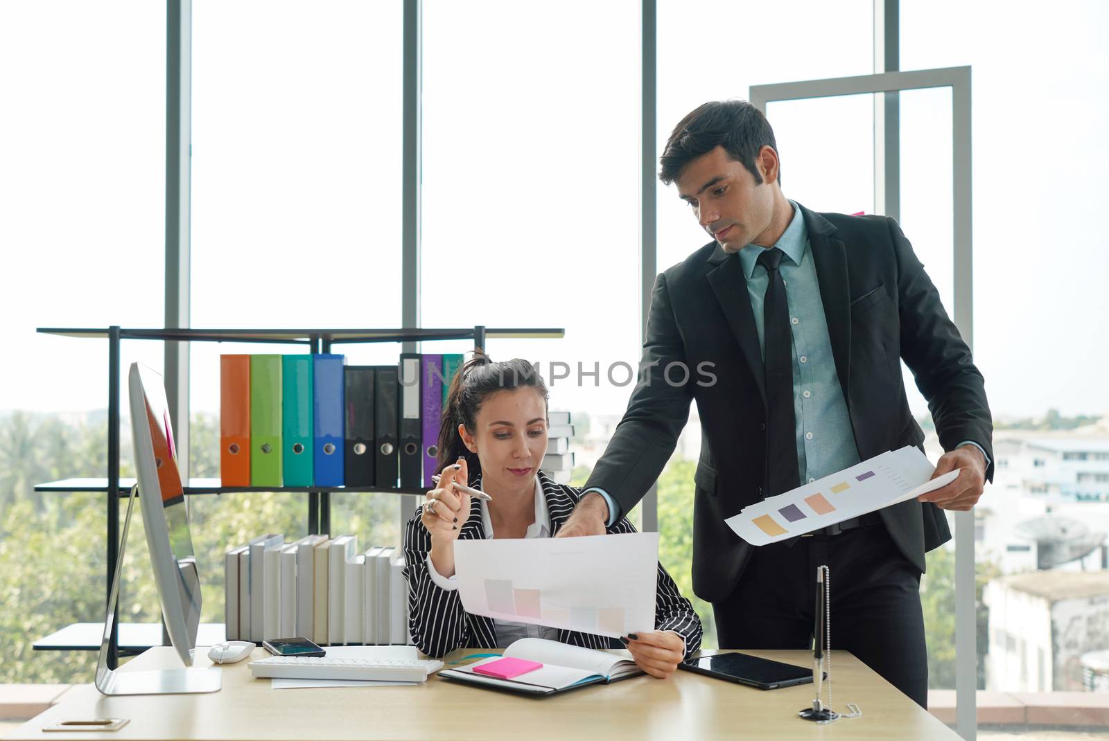 A young business man in a black suit is teaching colleagues about investment and profits in various forms. The secretary didn't understand what the employer was trying to explain to her.
