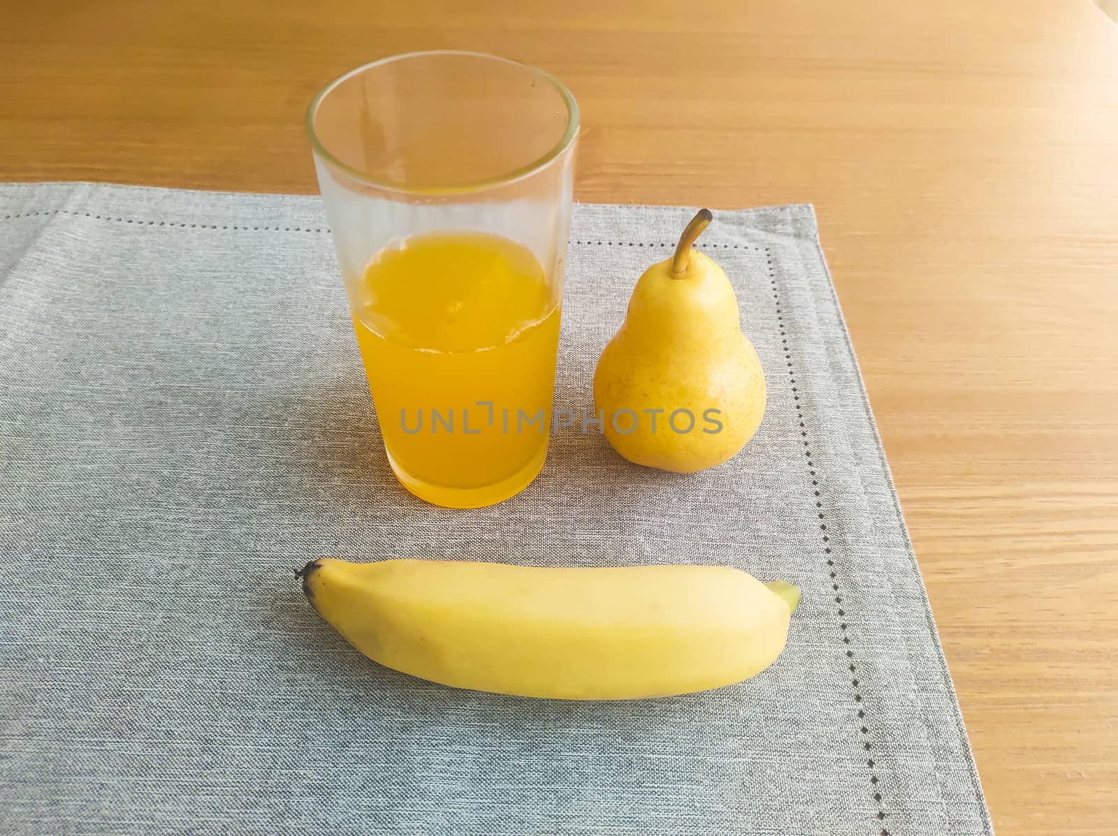 Banana, pear and glass of orange juice, on fabric towel, on the table and blurred background.