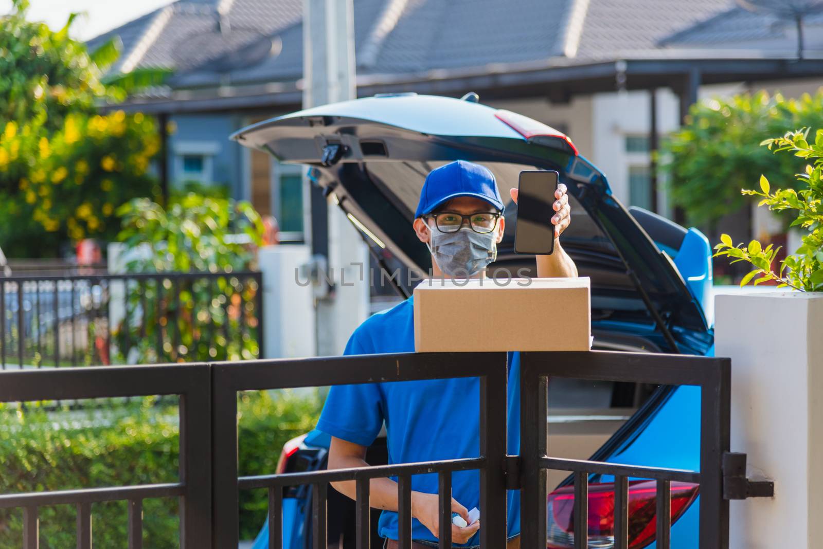 Asian delivery man courier Place deliveries boxes at home and showing mobile phone blank screen for customer sign he protective face mask service under curfew quarantine pandemic coronavirus COVID-19