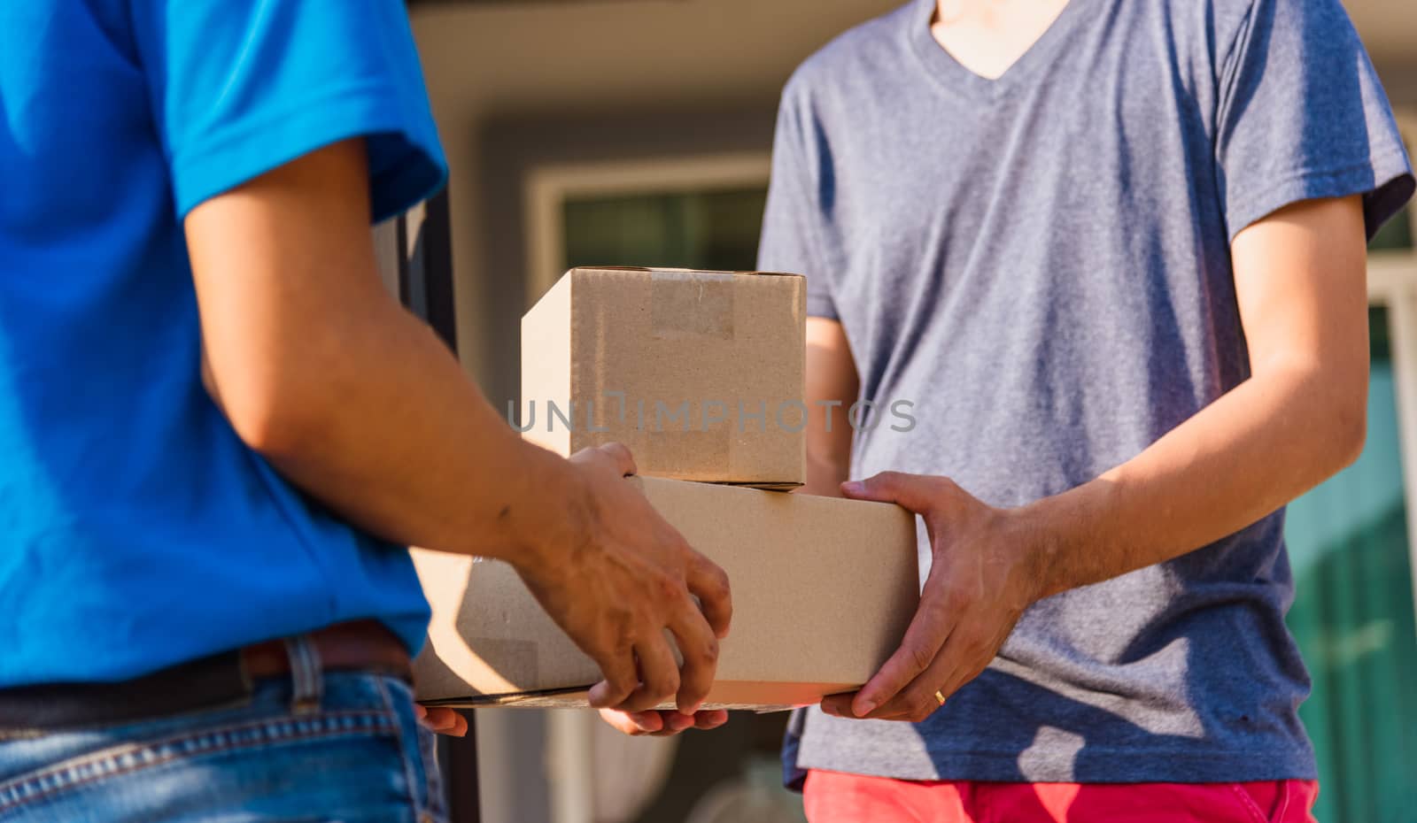 Asian Young delivery man courier with package post box in uniform he protective face mask he making service and customer receiving front house under curfew quarantine pandemic coronavirus COVID-19