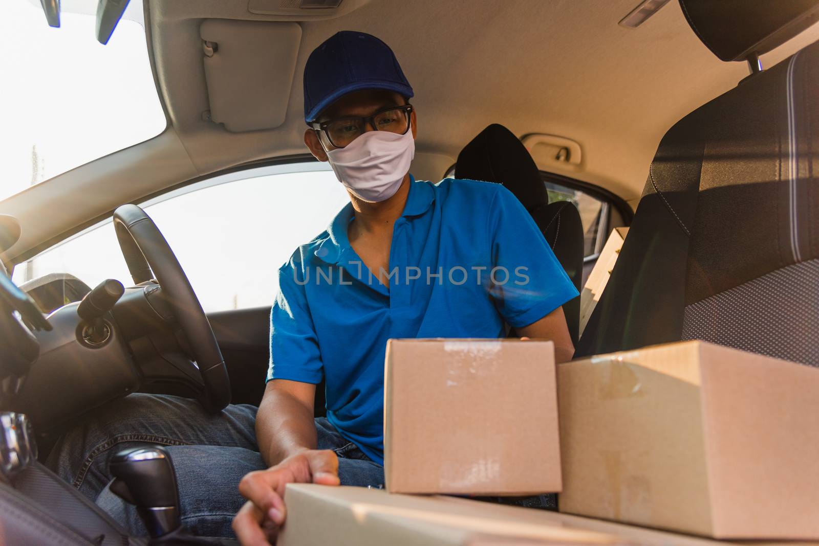 Asian Young delivery man courier online with boxes with uniform sitting in driving car he protective face mask, service customer on front house under curfew quarantine pandemic coronavirus COVID-19