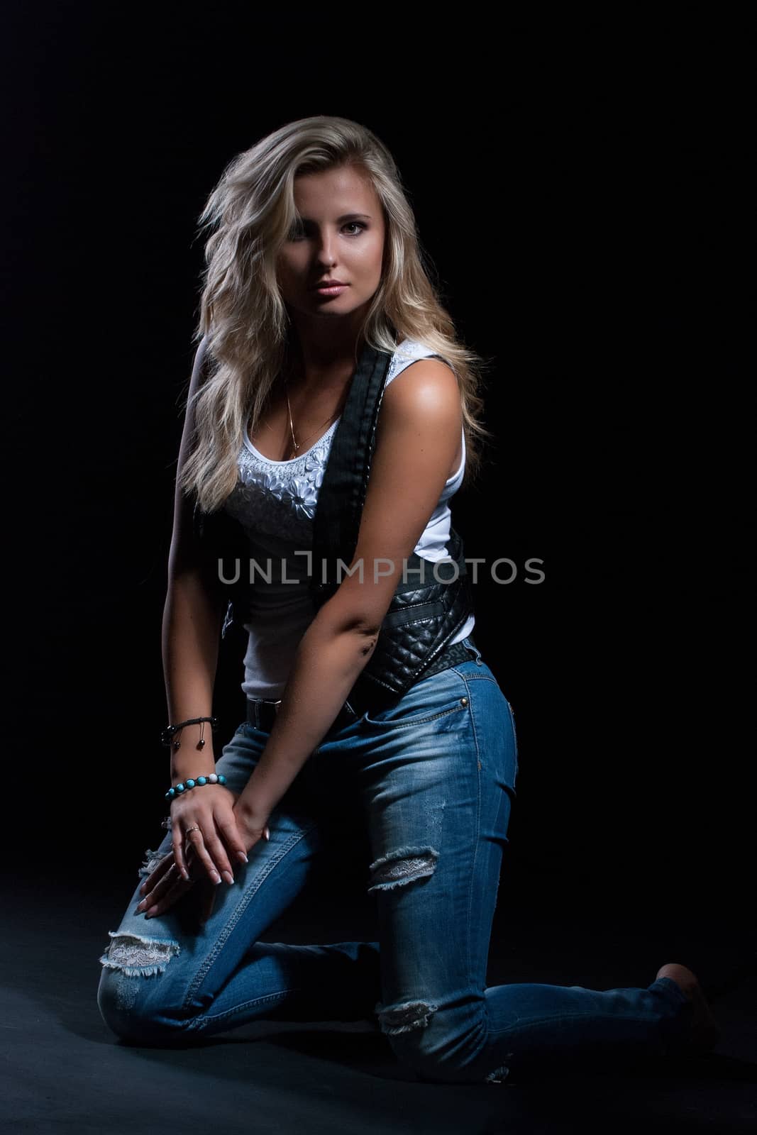 young, girl, blonde, jeans, clothes on a dark background kneels by Andreua