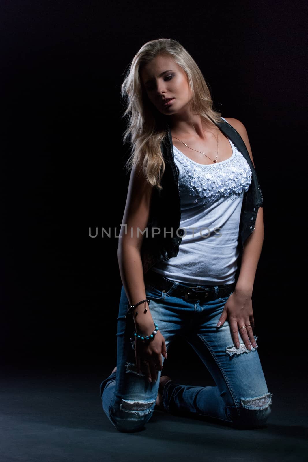 young, girl, blonde, jeans, clothes on a dark background kneels