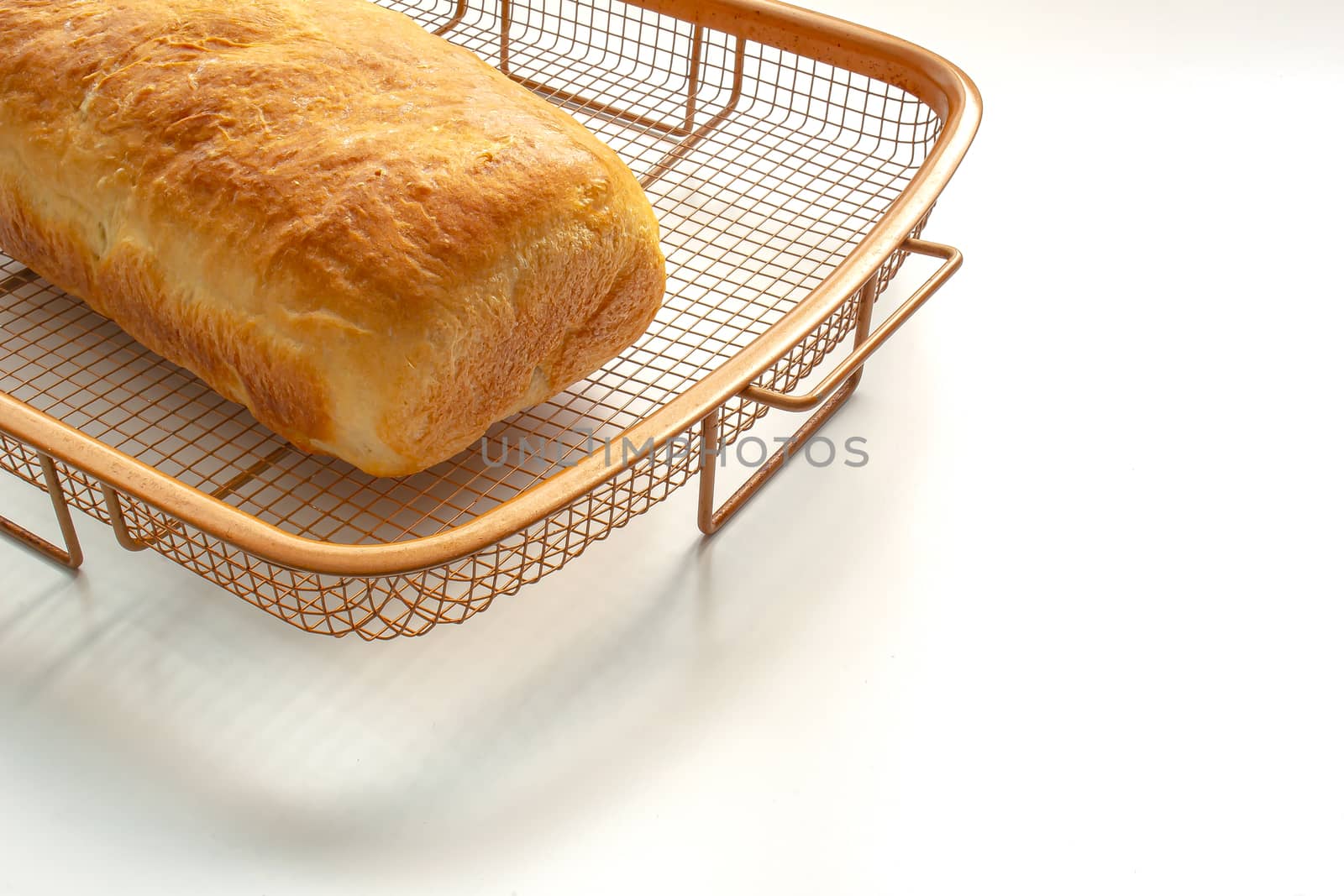 An isolated homemade white bread on a cooling rack on white table by oasisamuel