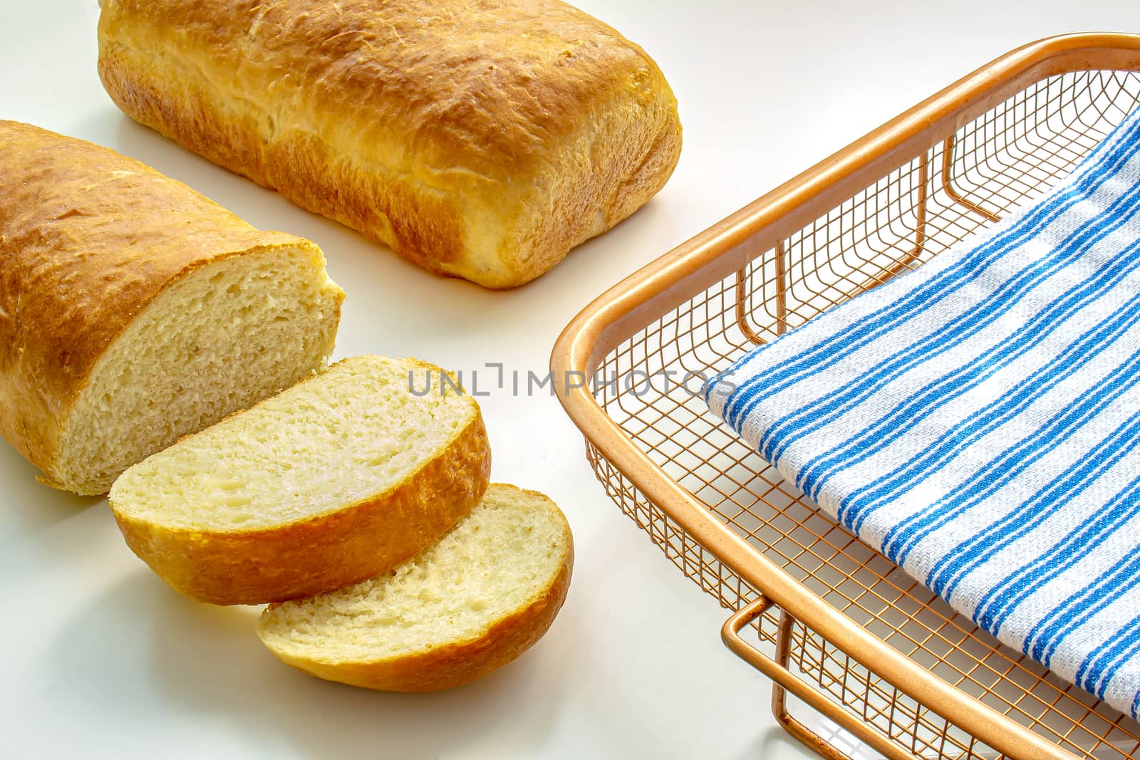 A slide homemade white bread on a cooling rack with a cloth on white table