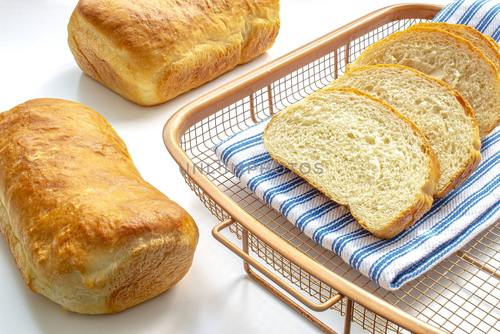 A couple of homemade white bread on a cooling rack with a cloth on white table by oasisamuel