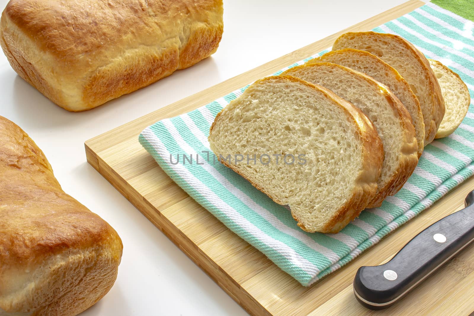 A couple of slide homemade white bread on a cooking wooden board with a cloth on white table by oasisamuel