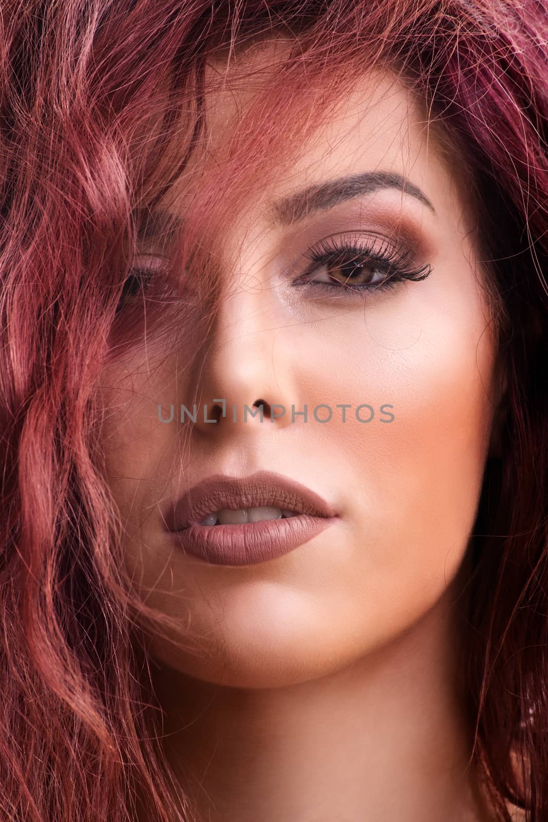 Close up portrait shot of a beautiful redhead young woman with dark smokey eye makeup and red lipstick with hair over her eye. Female fashion. Beautiful young woman with perfect skin and long hair.