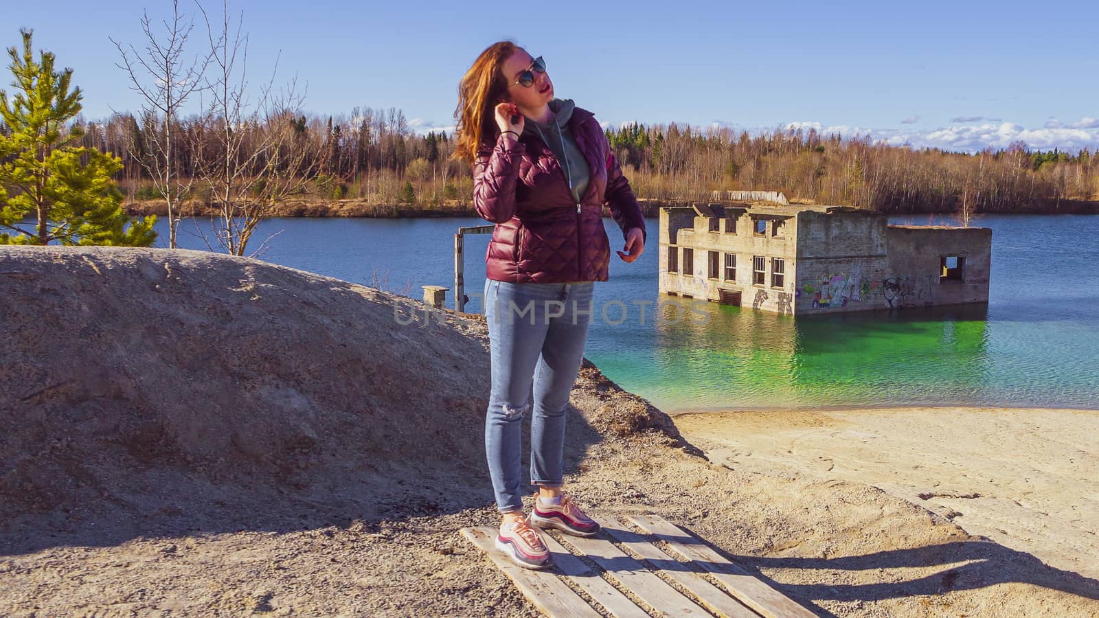 young woman with red jacket and abndoned Quarry Of Rummu, Estonia on the background. Scenic View Of Land Against Clear Blue Sky. Panoramic View.