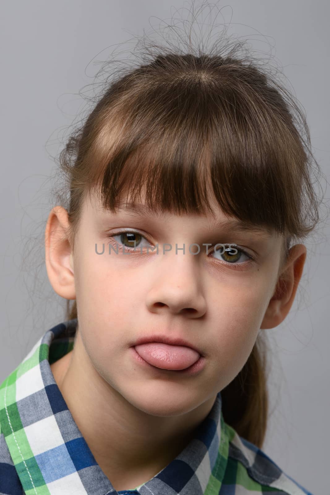 Portrait of a ten-year-old girl sticking out her tongue from resentment, European appearance, close-up