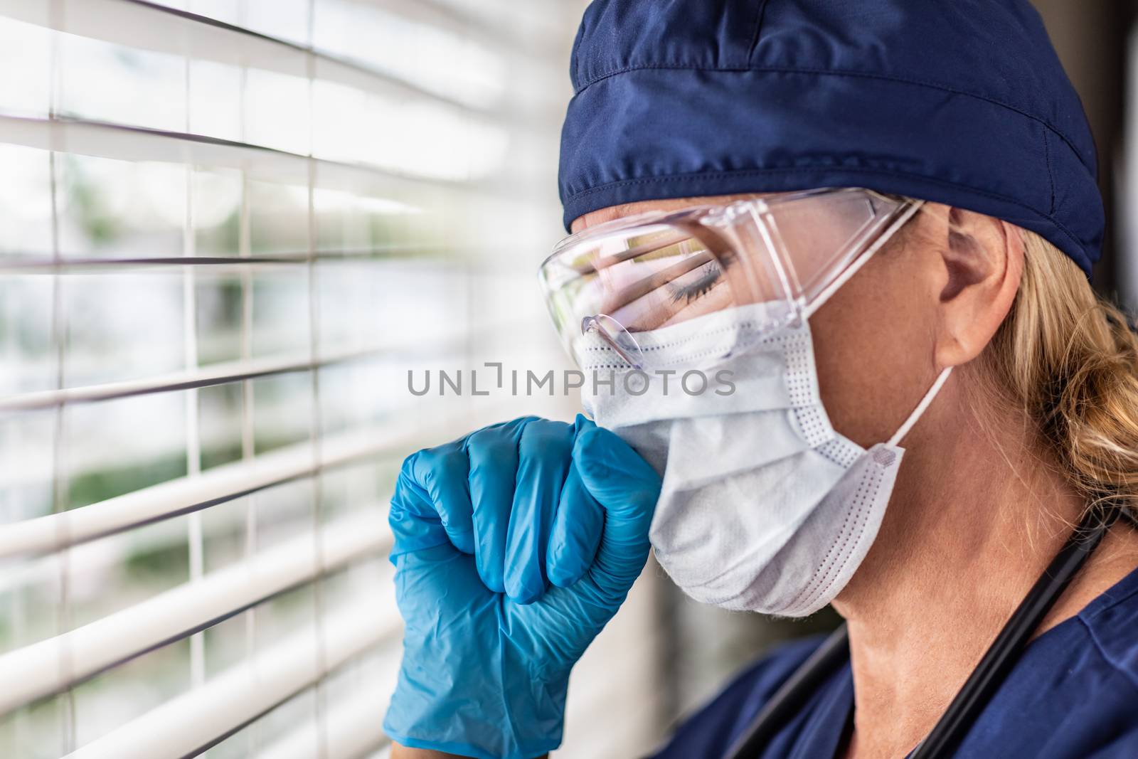 Female Doctor or Nurse On Break At Window Wearing Medical Face Mask and Goggles.