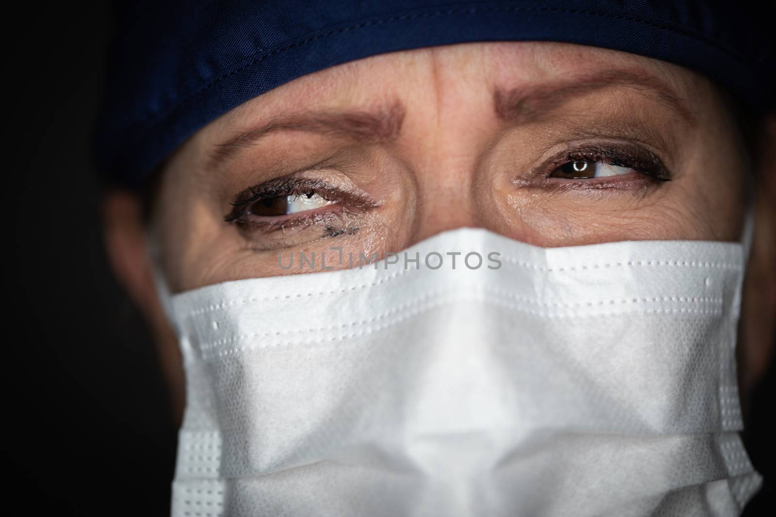 Tearful Stressed Female Doctor or Nurse Wearing Medical Face Mask on Dark Background. by Feverpitched