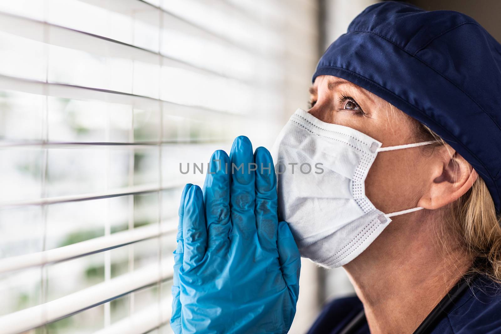 Prayerful Stressed Female Doctor or Nurse On Break At Window Wearing Medical Face Mask.
