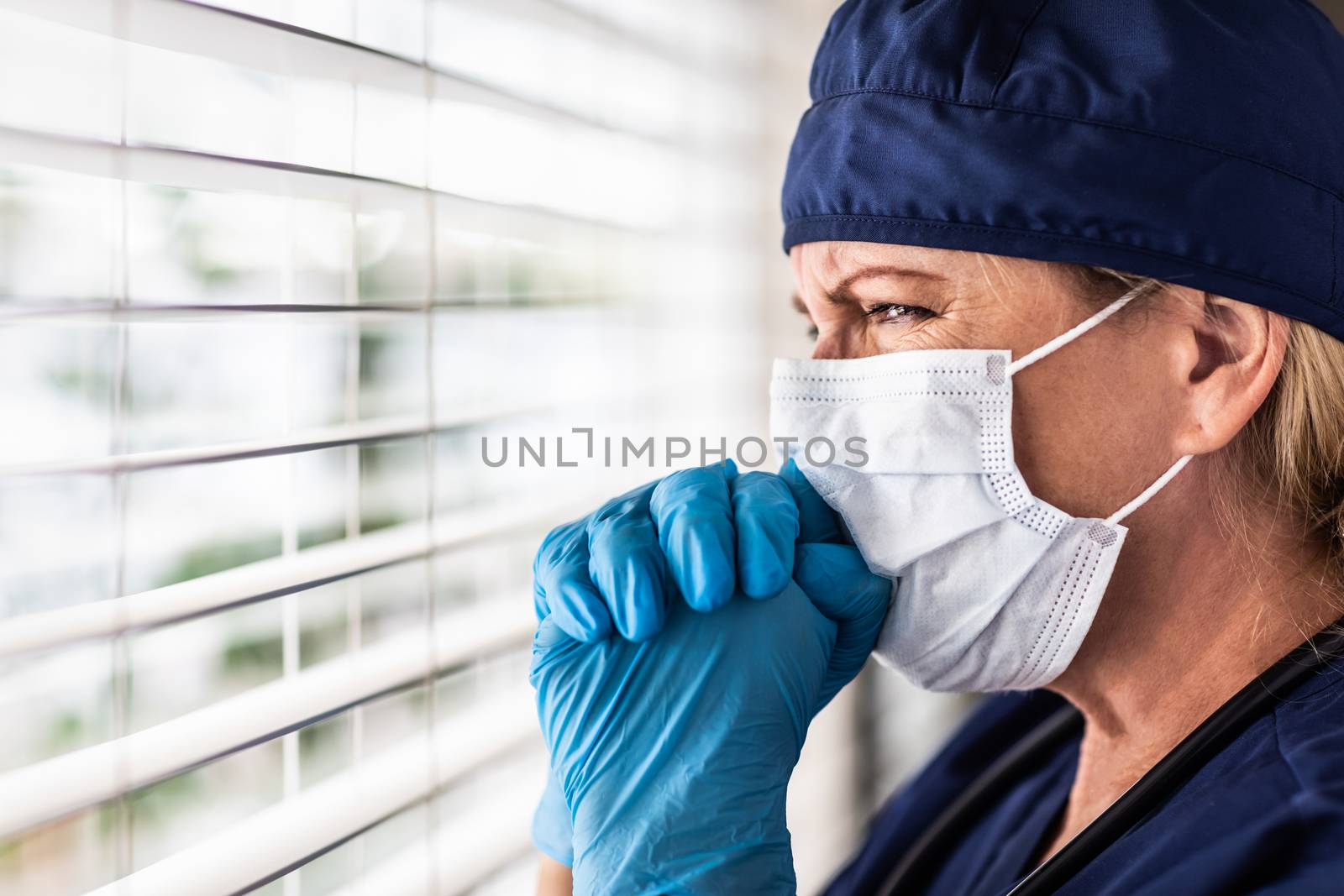 Prayerful Stressed Female Doctor or Nurse On Break At Window Wearing Medical Face Mask.