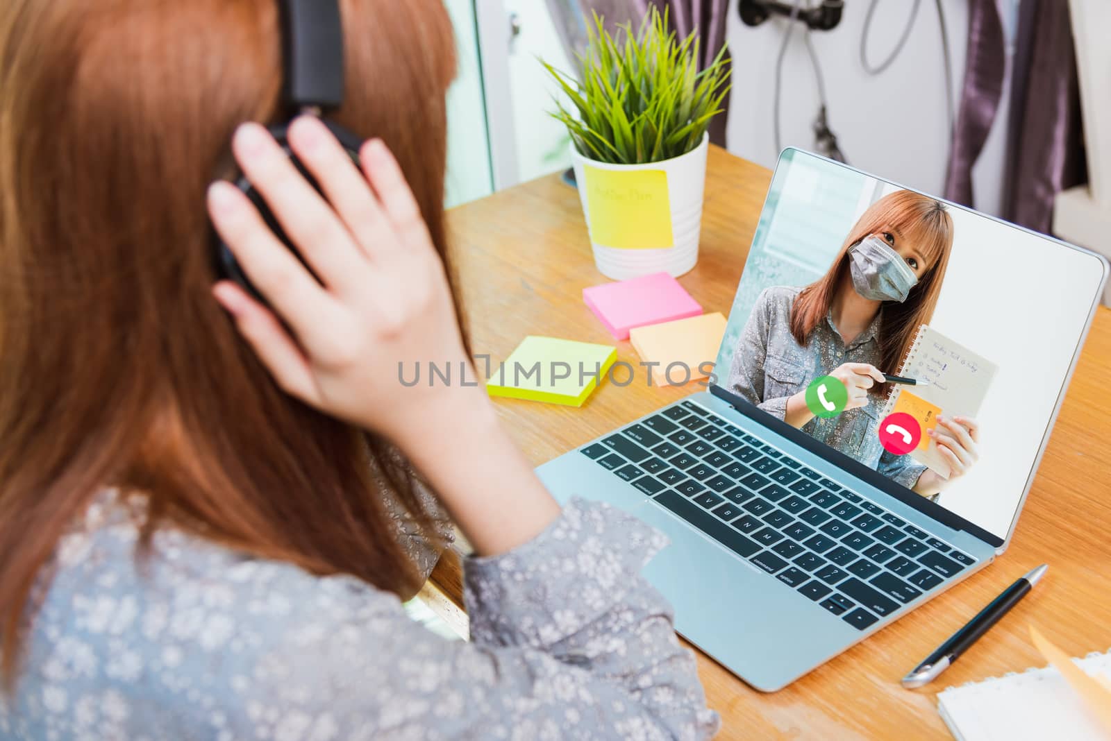 Back view of Asian business woman smart work from home using laptop computer call online to meeting talking plan in webcam video conference under curfew quarantine pandemic coronavirus COVID-19