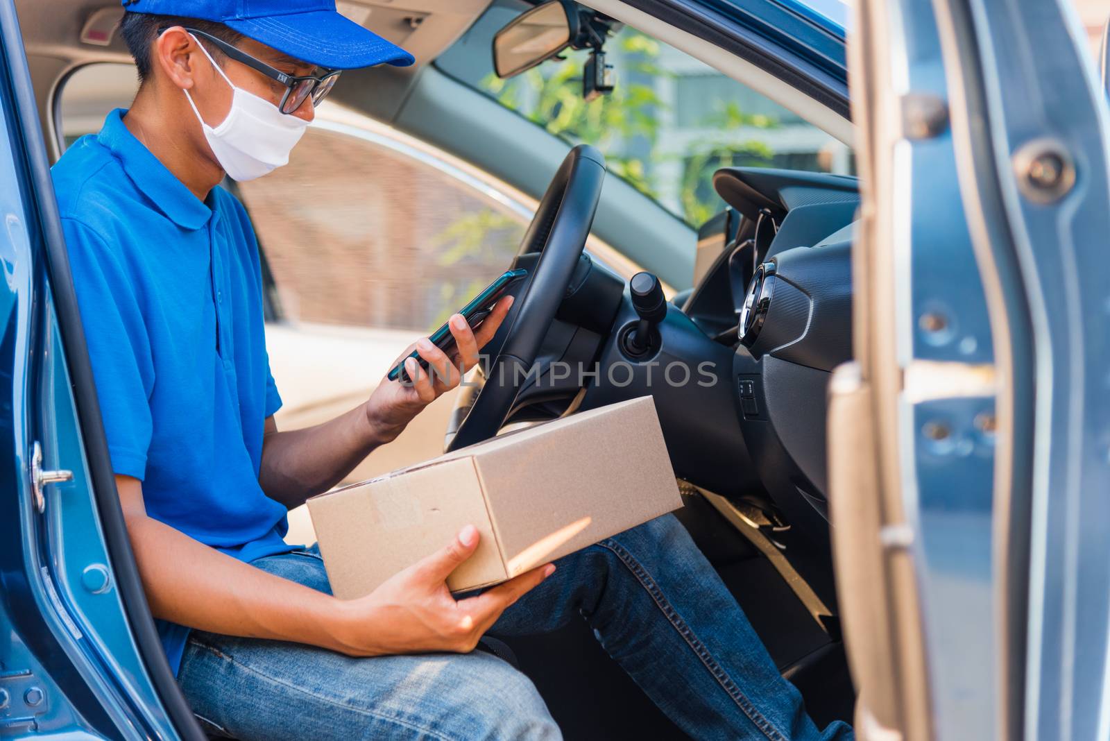 Asian delivery man courier online holding deliveries out boxes in car and using mobile phone contact the customer he protective face mask service under curfew quarantine pandemic coronavirus COVID-19