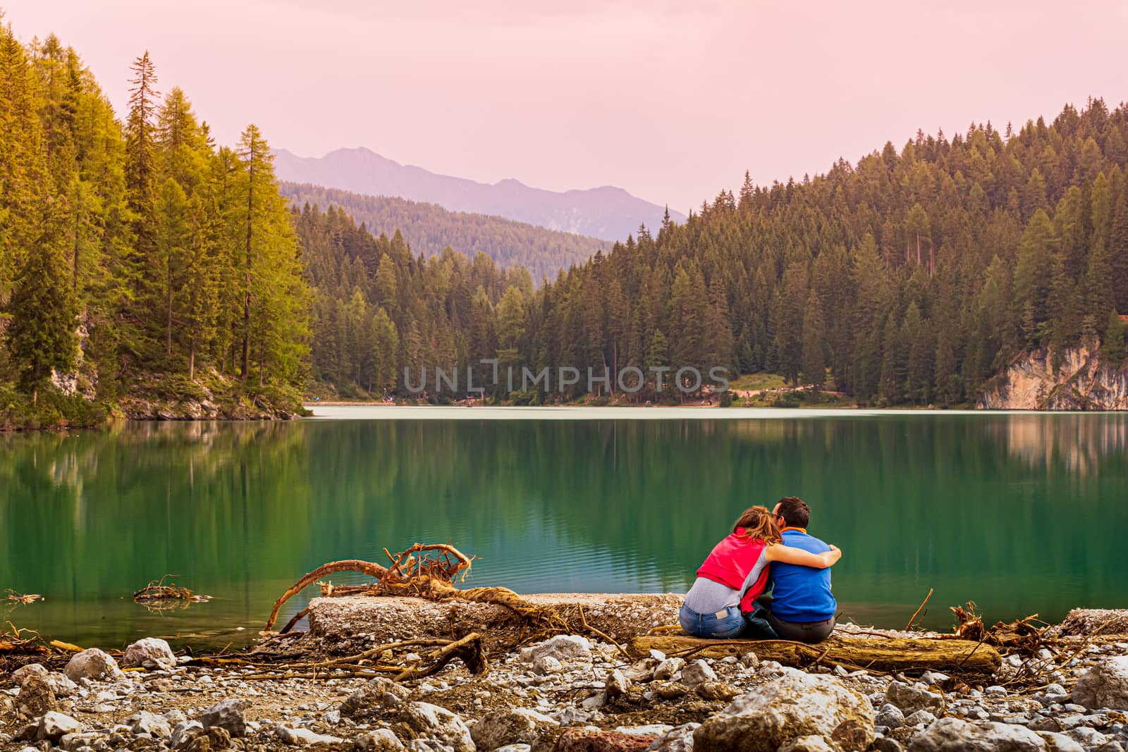 Loving couple sitting on the edge of the Pragser Wildsee by brambillasimone