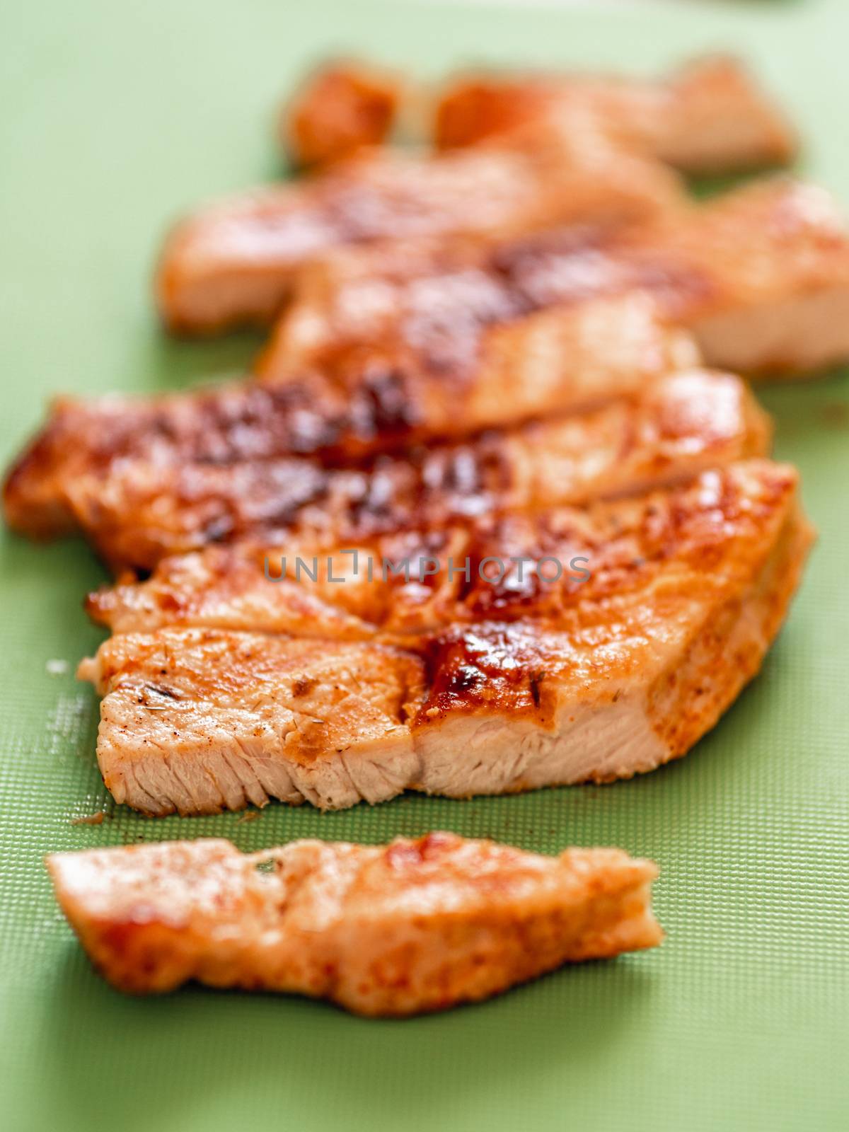 Grilled turkey meat steak sliced on cutting board over wooden tabletop. Perfect ready-to-eat turkey fillet on green cutting board. Striped cooked fillet of turkey meat. Vertical. Copy space