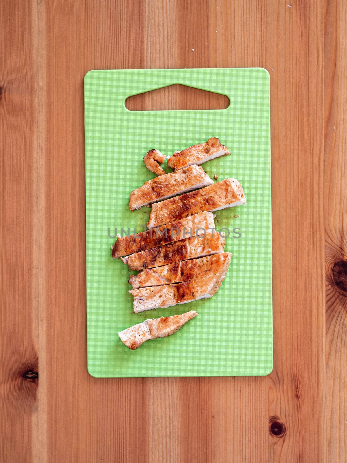 Grilled turkey meat steak sliced on cutting board over wooden tabletop. Perfect ready-to-eat turkey fillet on green cutting board top view or flat lay. Striped cooked fillet of turkey meat. Vertical