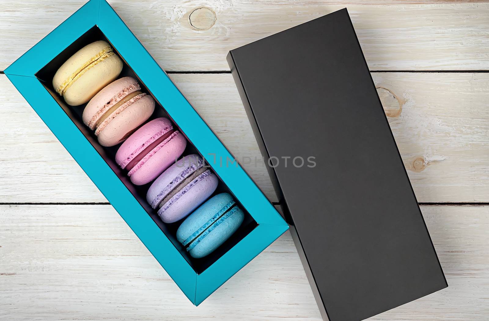 Macaroons in box next to lid on wooden background