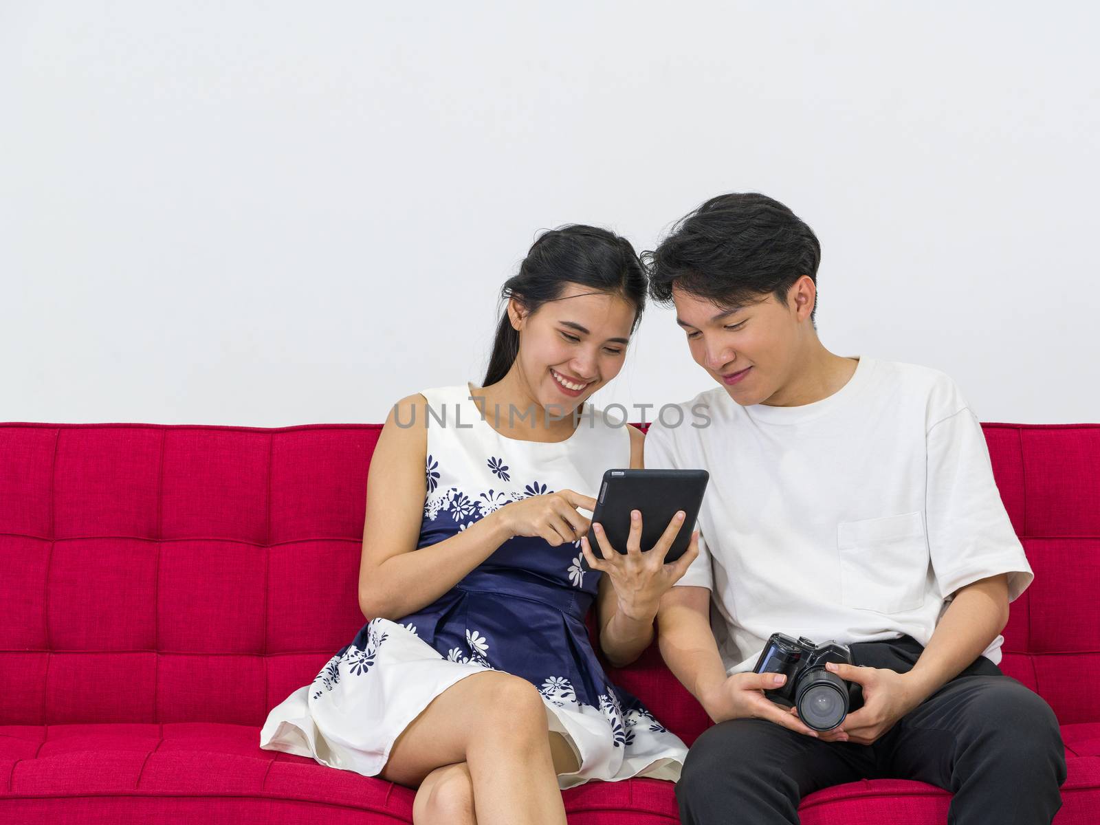 Asian photographers allow models to view pictures taken on the tablet computer screen while sitting on a red sofa. Working atmosphere in the photo studio