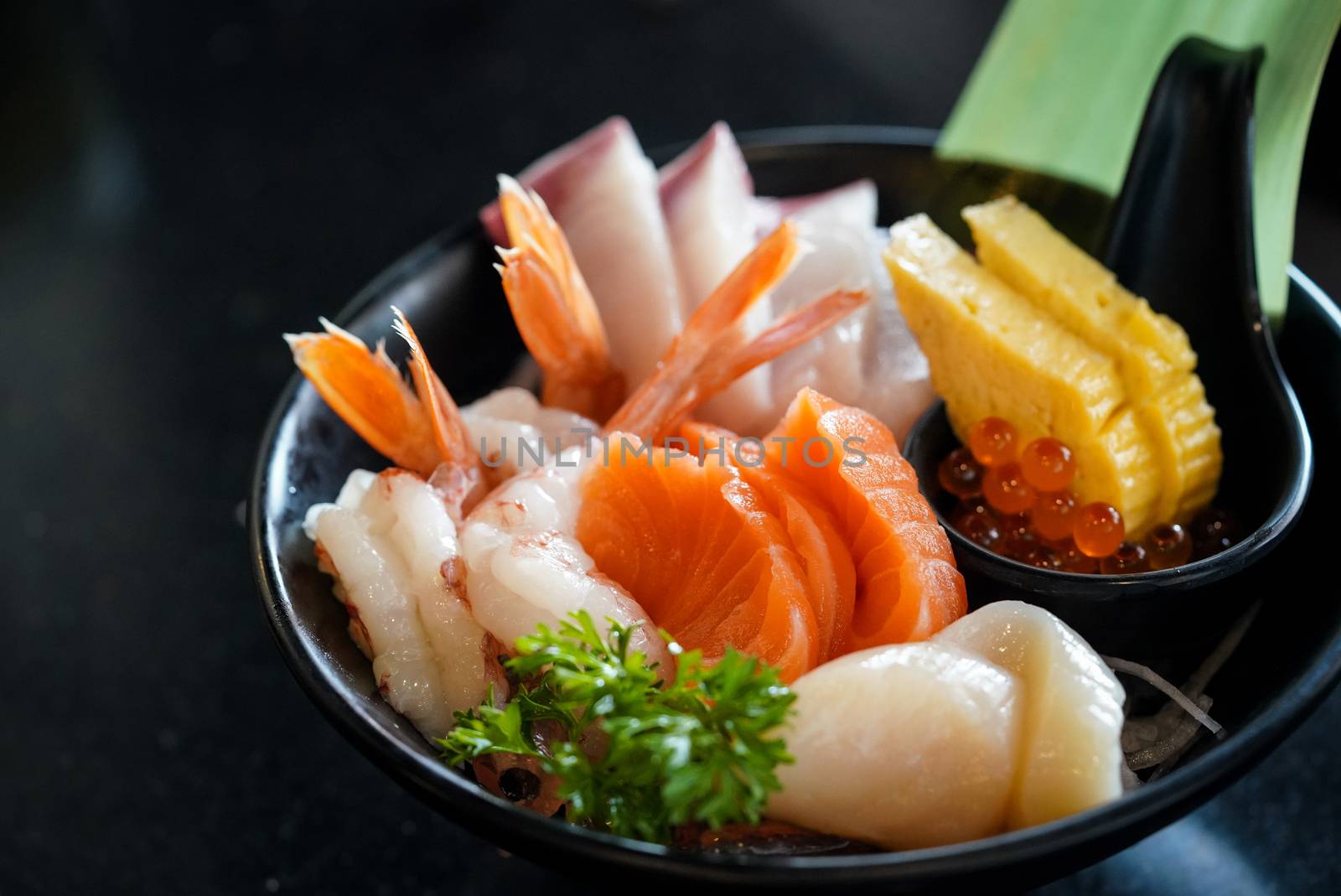 The sashimi set is beautifully arranged in a black plate decorated with green leaves. Japanese Cuisine Buffet. Chef's Choice: Salmon, hamachi, scallops, shrimp, tamagoyaki and flying fish roe.