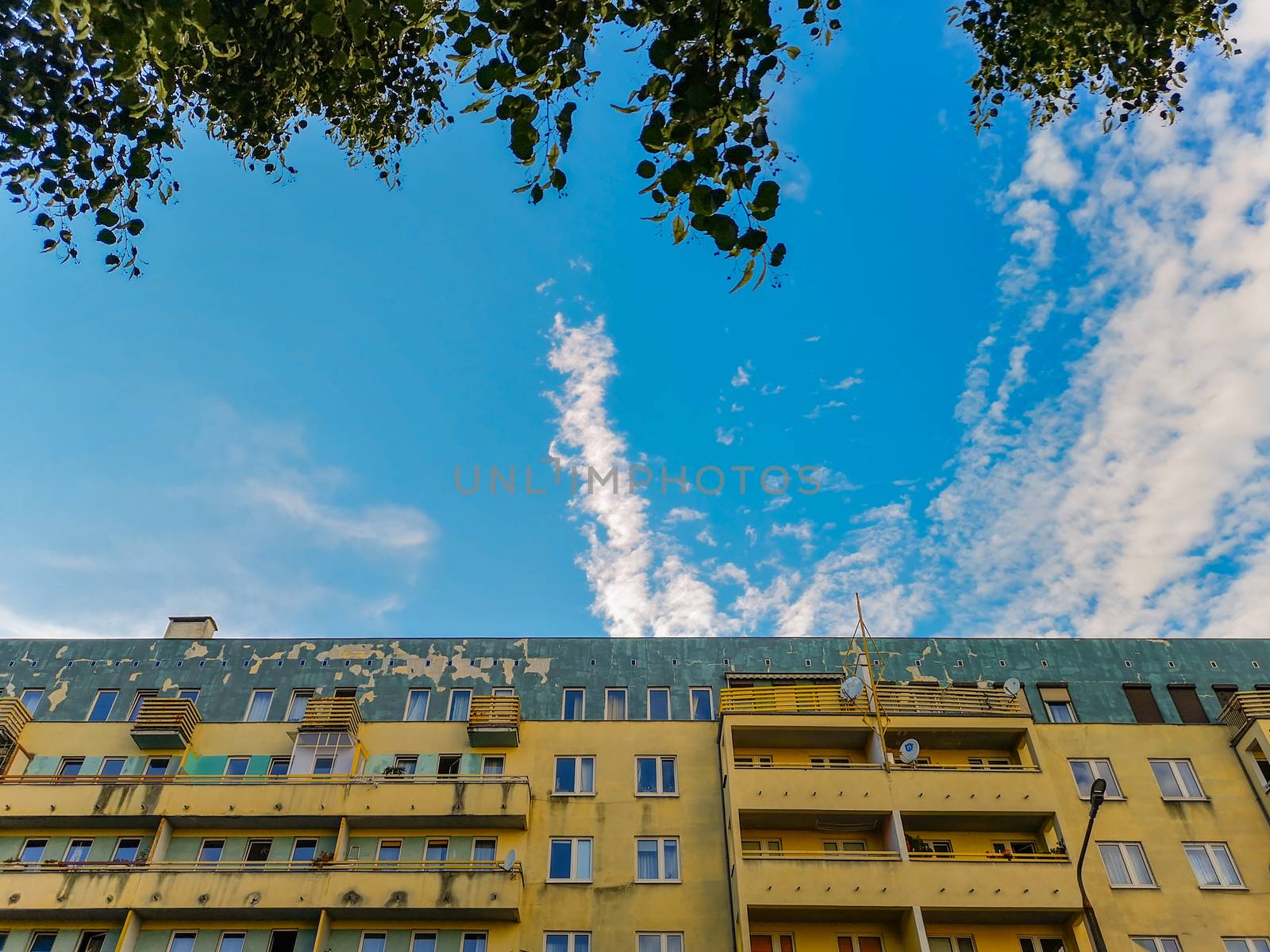 Cloudy sky between tree branches and colorful residential building in Wroclaw City by Wierzchu