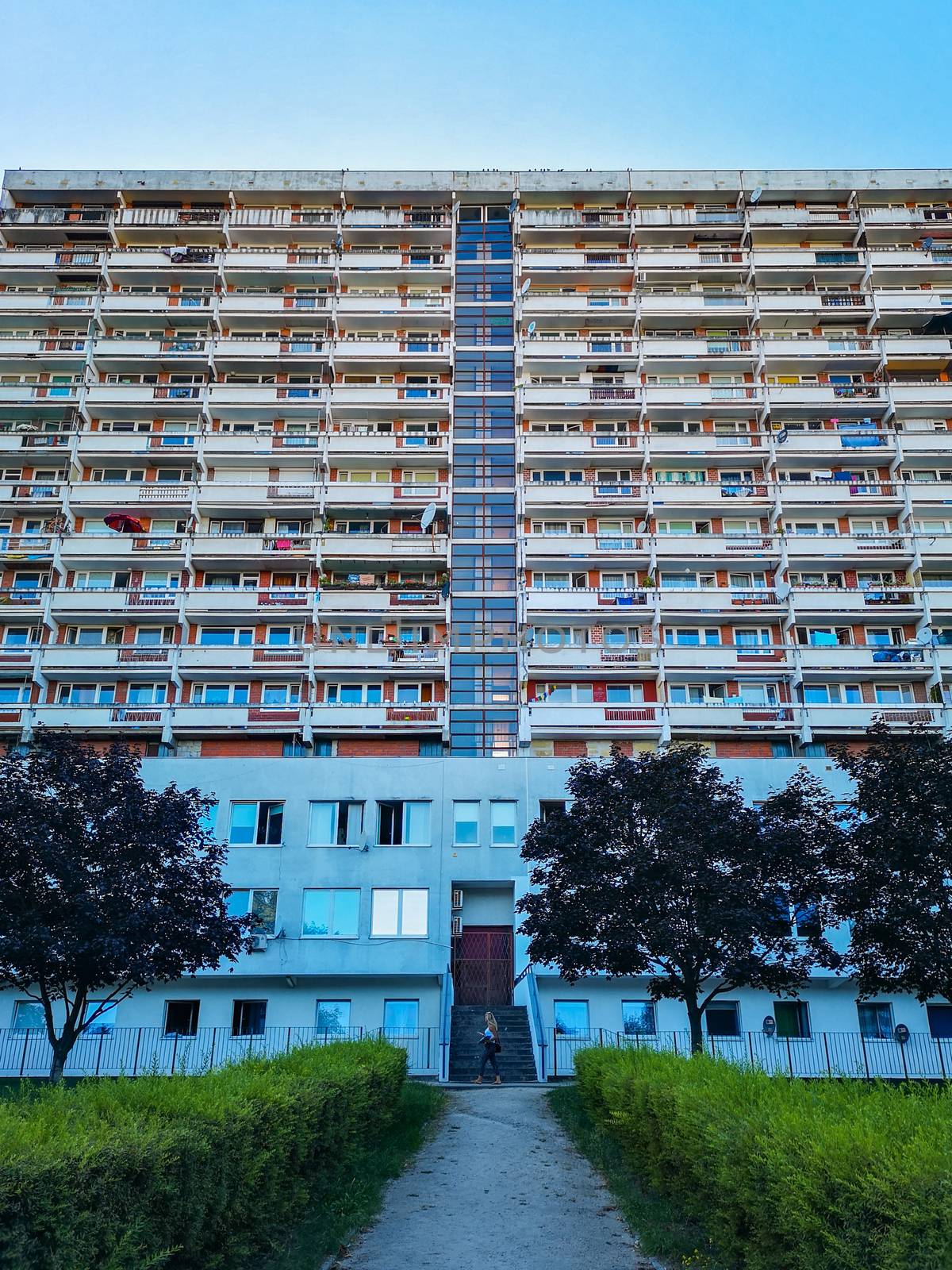 Symmetrical look to residential building with small park in front of and walking woman in center