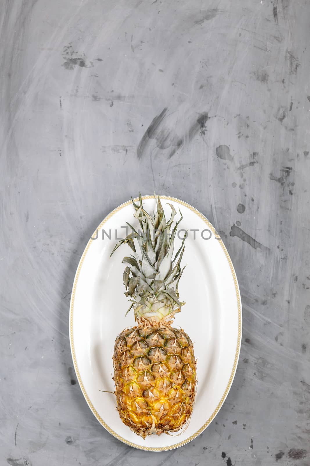 White Plate with Ripe Whole Pineapple on Grey Concrete Background. Copyspace.