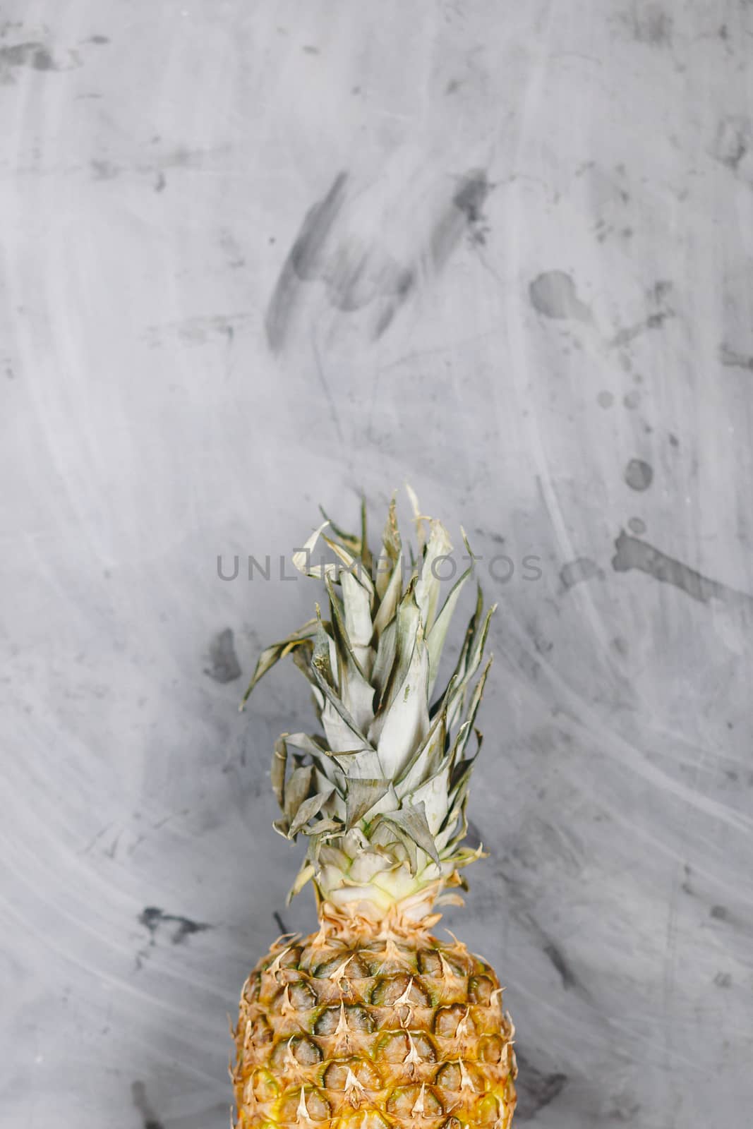 White Plate with Ripe Whole Pineapple on Grey Concrete Background. Copyspace.