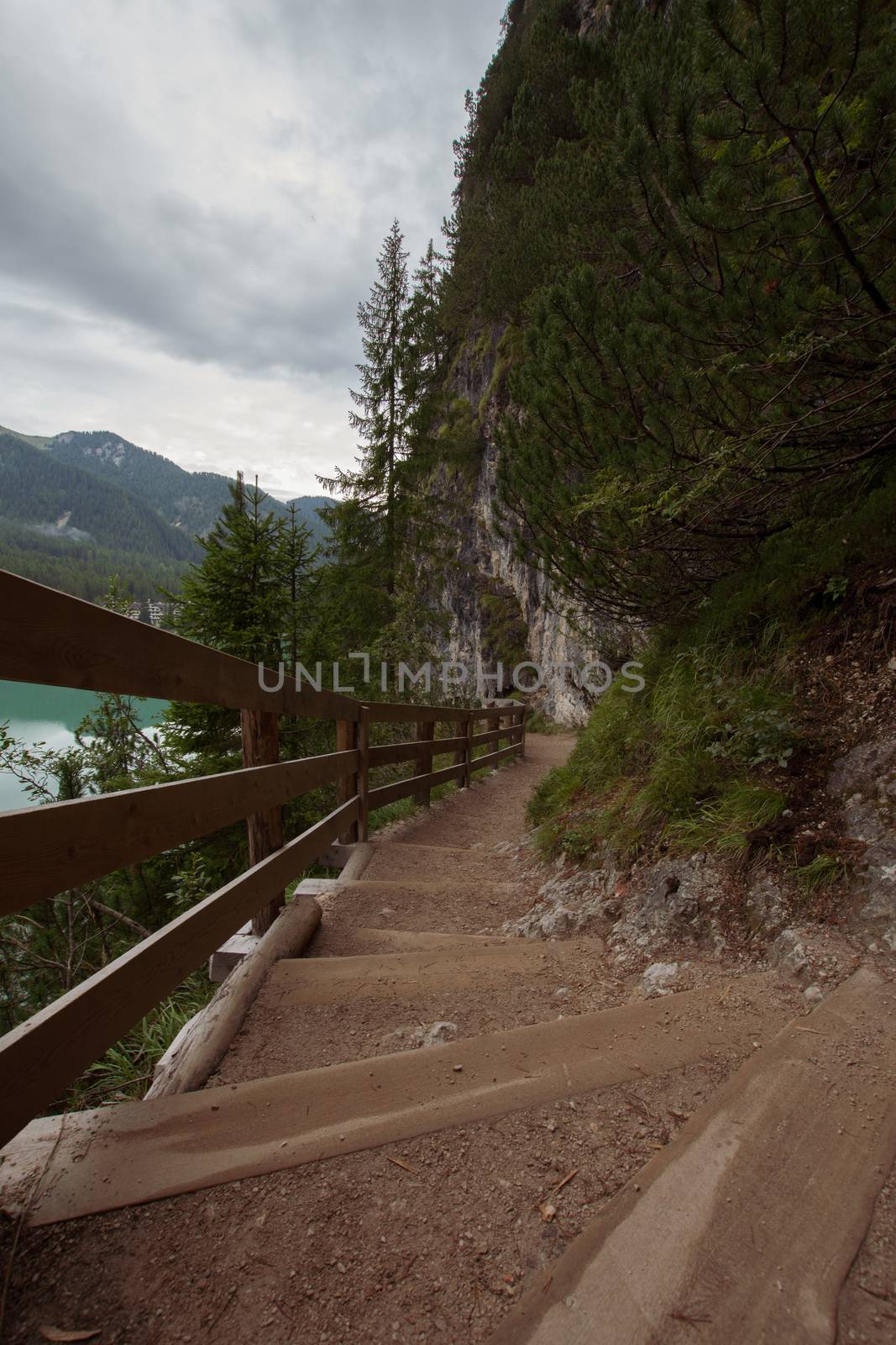 Dirt path to staircase runs along the Braies Lake under a cloudy by brambillasimone