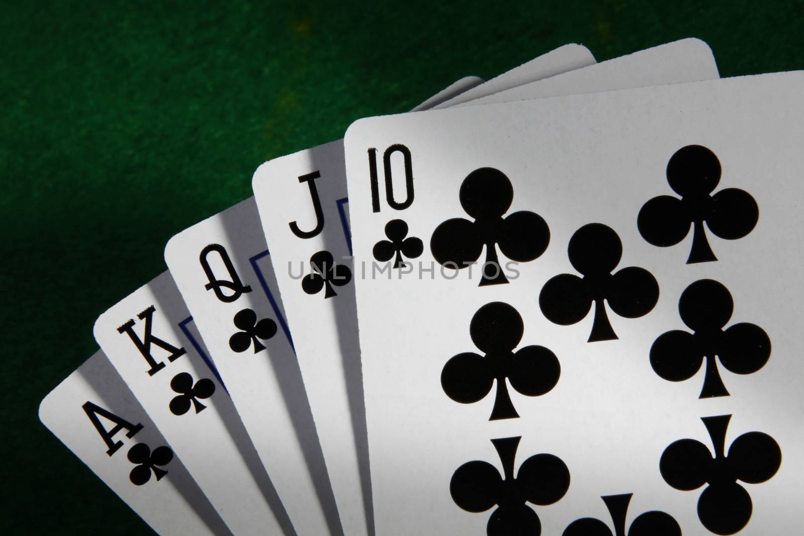 A Royal Flush in Clubs highest poker hand with green card table background and moody light