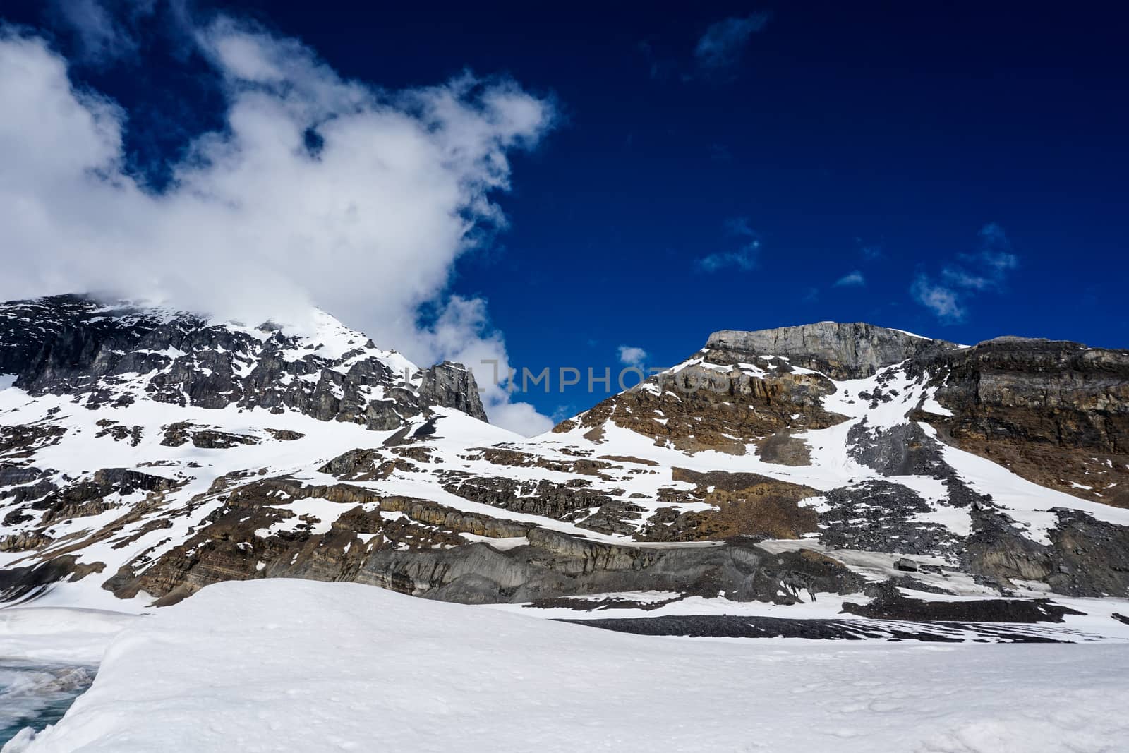 Snowcapped Canada's Rockies mountain during a summer day contrasting with a bright blue sky and white clouds by sonandonures