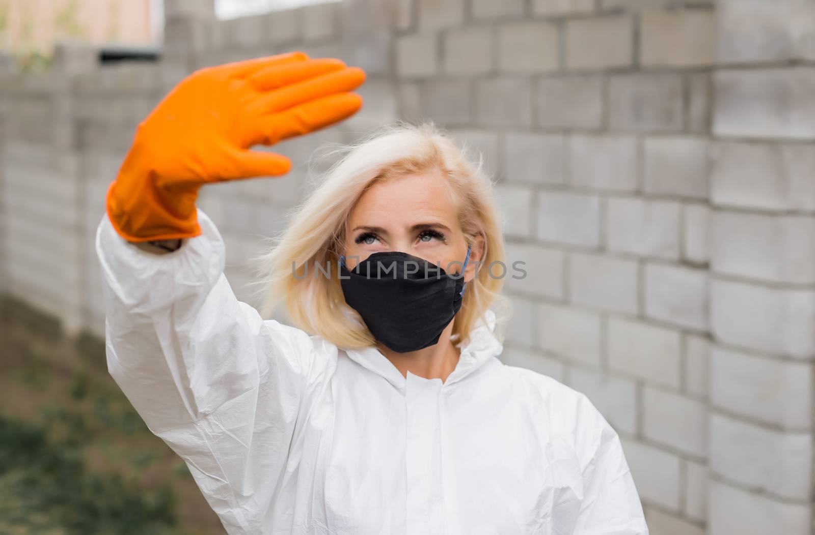 Woman in black mask, white protective suit and gloves making sigh stop