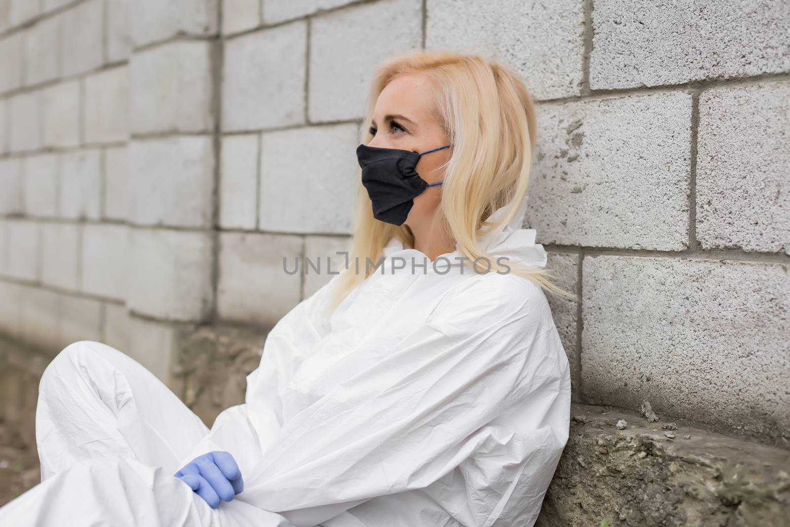 Woman in black mask, white protective suit and gloves sitting against wall by Angel_a