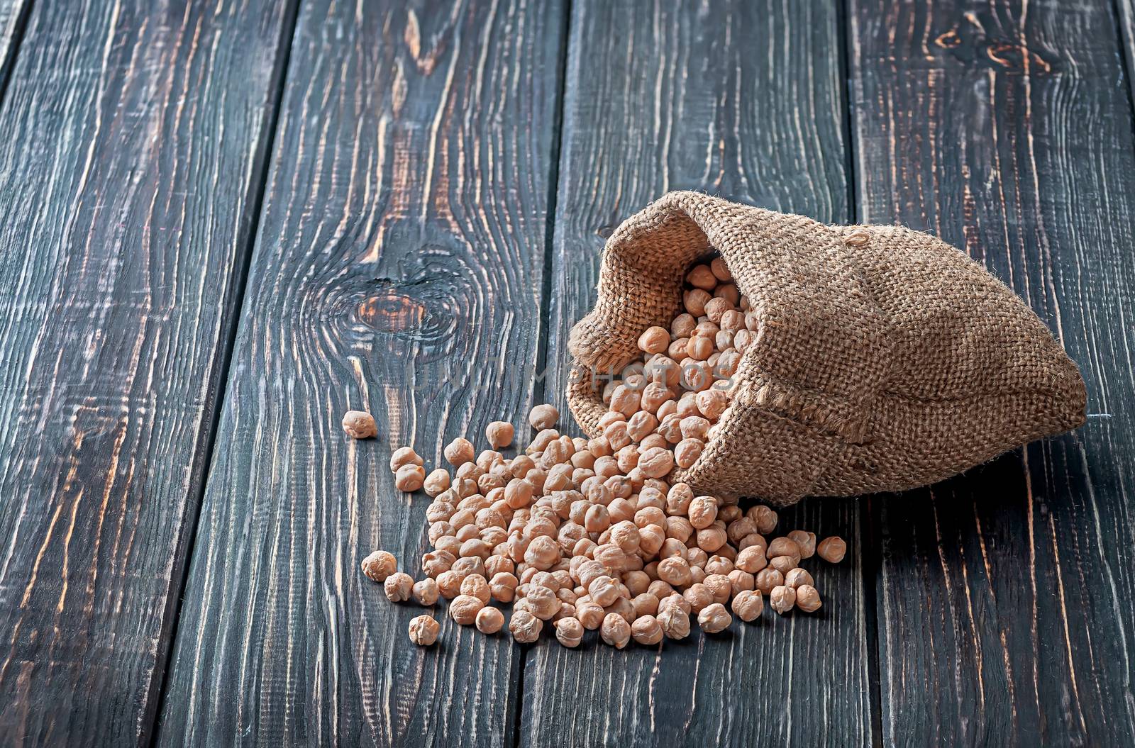 Chickpea spill out of the bag on wooden background