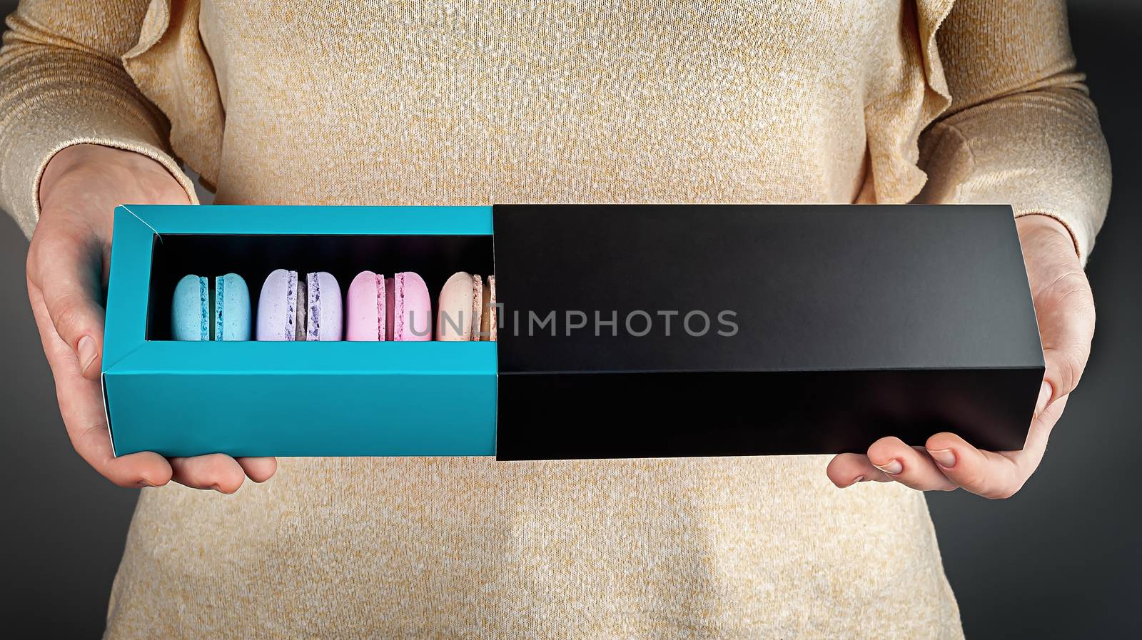 Beautiful female hands hold multicolored french macaroons in gift box