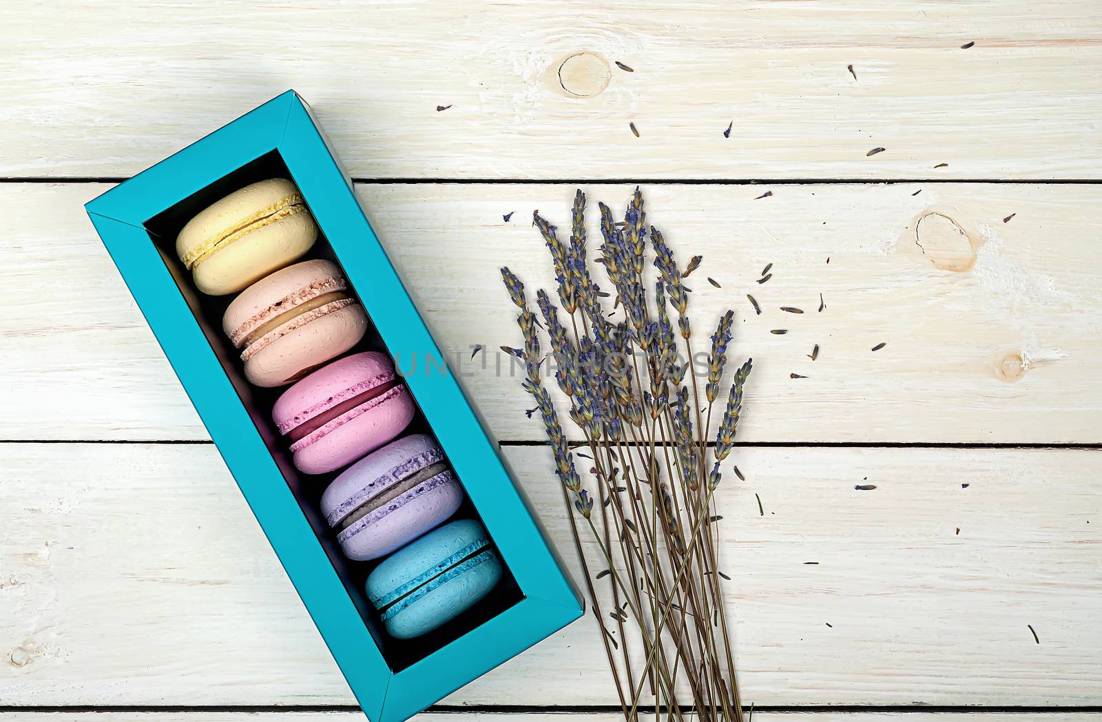Macaroons in gift box next to lavender on wooden background