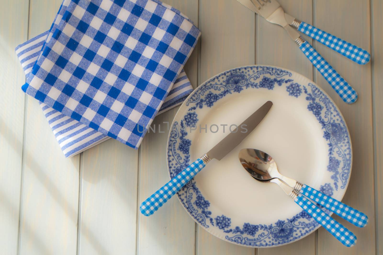 Empty plate, silverware and towel over wooden table background. View from above, blue color