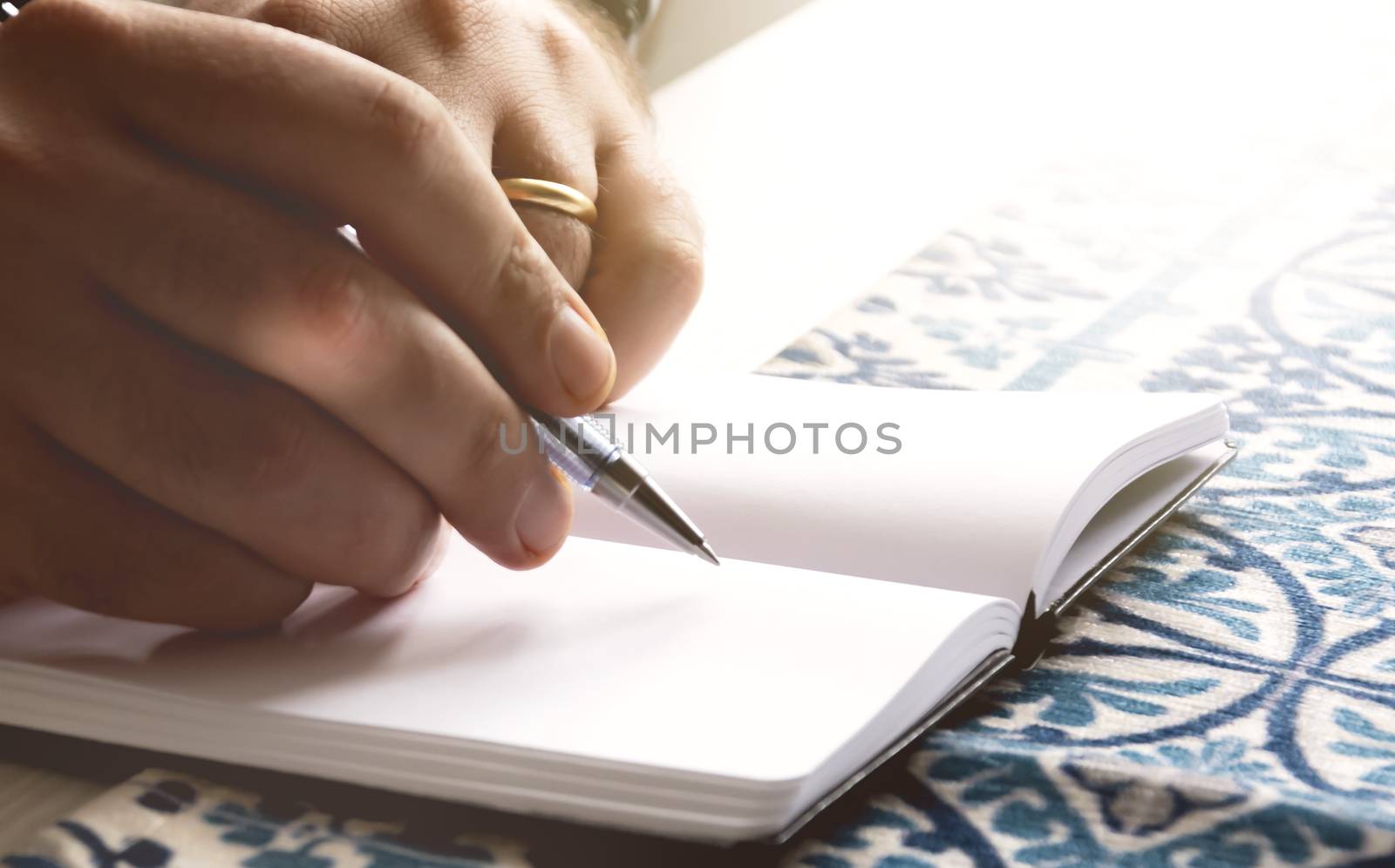 male hands holding a ballpoint pen to write on the blank pages of an open notebook. by rarrarorro