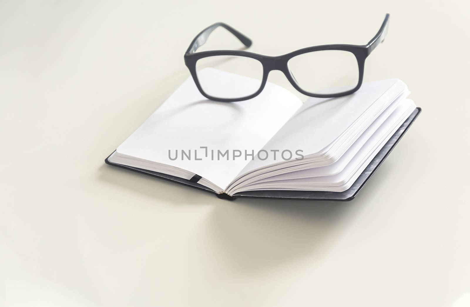 a pair of eyeglasses on an open notebook with blank pages. by rarrarorro