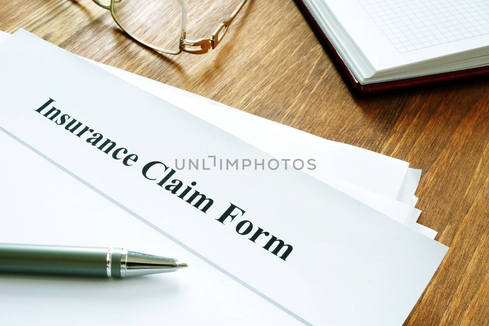 Insurance claim form with pen on wooden surface. by designer491
