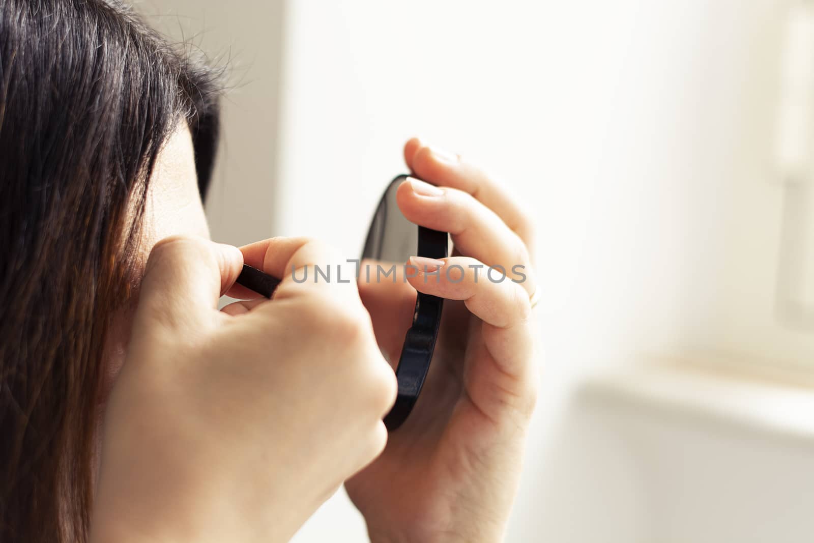 Female person using tweezers and a mirror with natural light. Personal care and beauty. Makeup accessories