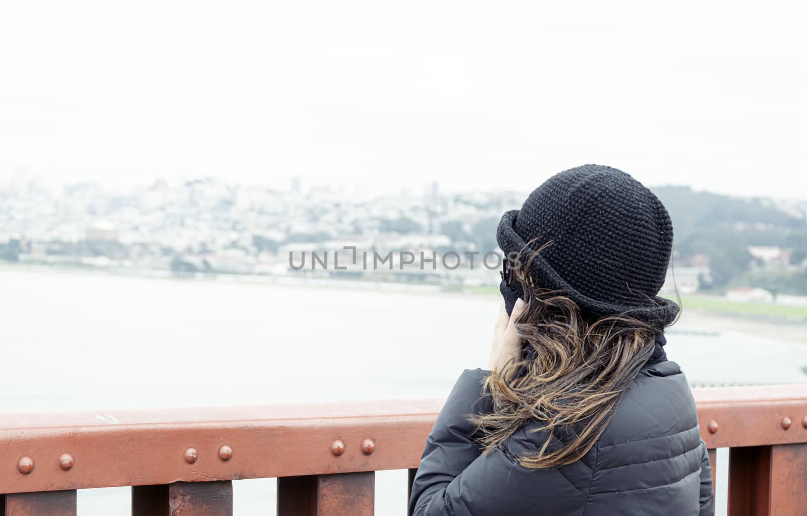 woman seen from behind while looking at the panorama of the San Francisco Bay from the Golden Gate Bridge on a cold and windy winter day