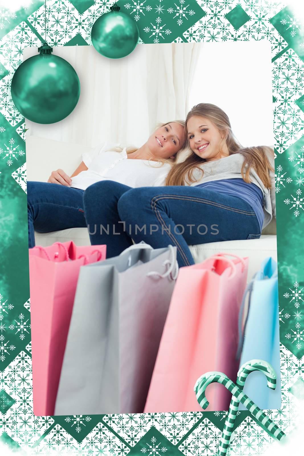 Smiling girls sitting on the couch with their bags of shopping against christmas frame
